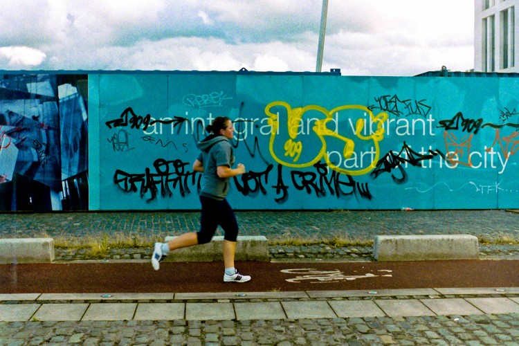 Woman running past hoarding with graffiti in Dublin docklands